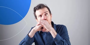 Man wearing dark blue shirt sitting and making a thinking face looking upwards with hands covering his mouth