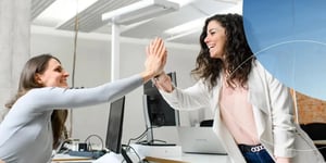 two women smiling and giving each other high five across table 