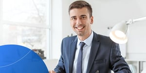 Man in suit sitting at desk and smiling into camera