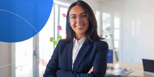 Woman in suit and glasses standing with arms crossed and smiling into camera 
