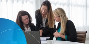 Three female employees sitting at desk and discussing with laptop in front of them