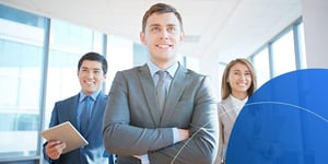 Man in suit with arms crossed smiling stand in front of two people behind him 