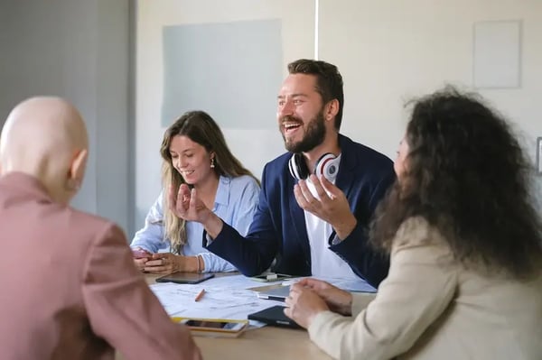 Employees sitting around table with one male employee smiling and gesturing