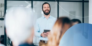 Man standing in front of crowd holding a tablet and smiling 