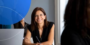 Woman sitting at desk holding pen in her hand and smiling away from camera