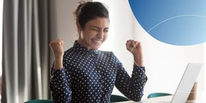 Woman sitting at desk with hands in fist and eyes closed showing excitement 