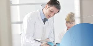 man in lab coat pointing to a book and explaining to his female colleague
